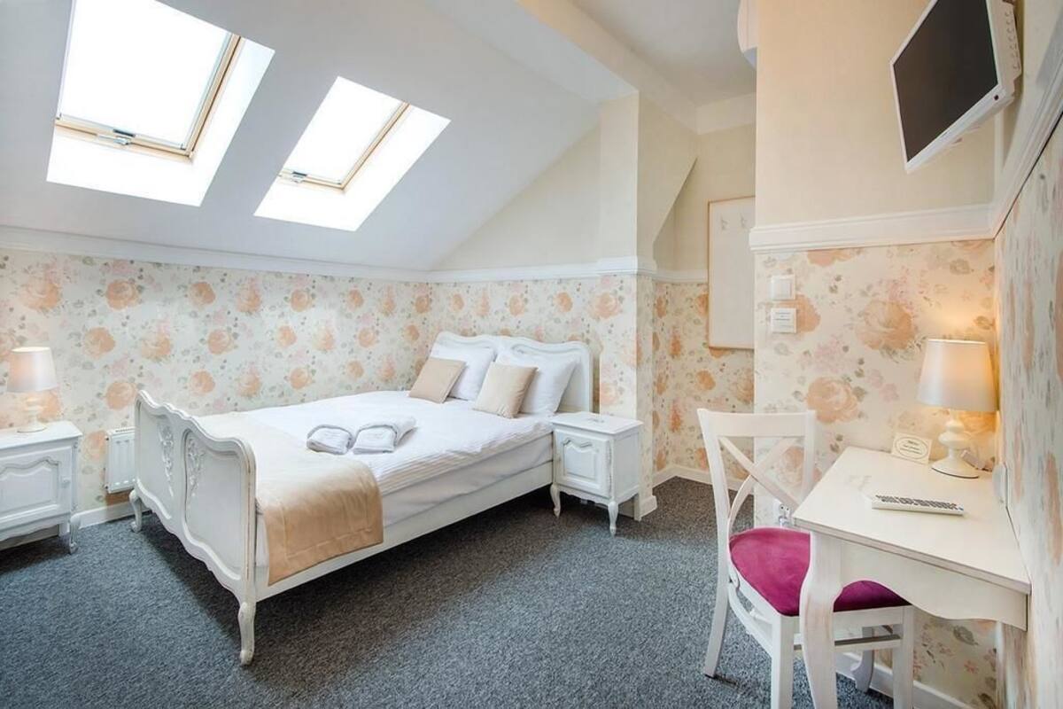 A bedroom with a bed, bedside tables, a desk, and a chair. There are two skylights on the ceiling.