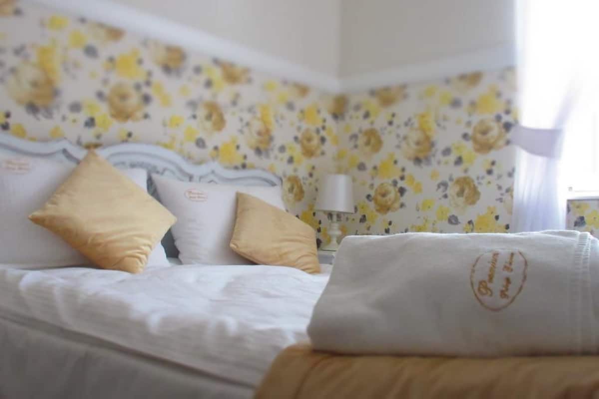 A hotel room with a bed, two pillows, a folded towel, and a floral wallpaper.