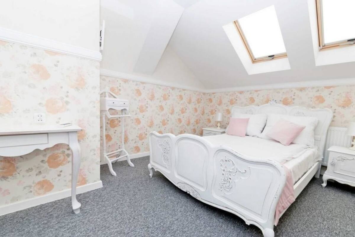 A bedroom with a white bed, a desk, and a dresser. There is a window on the ceiling.