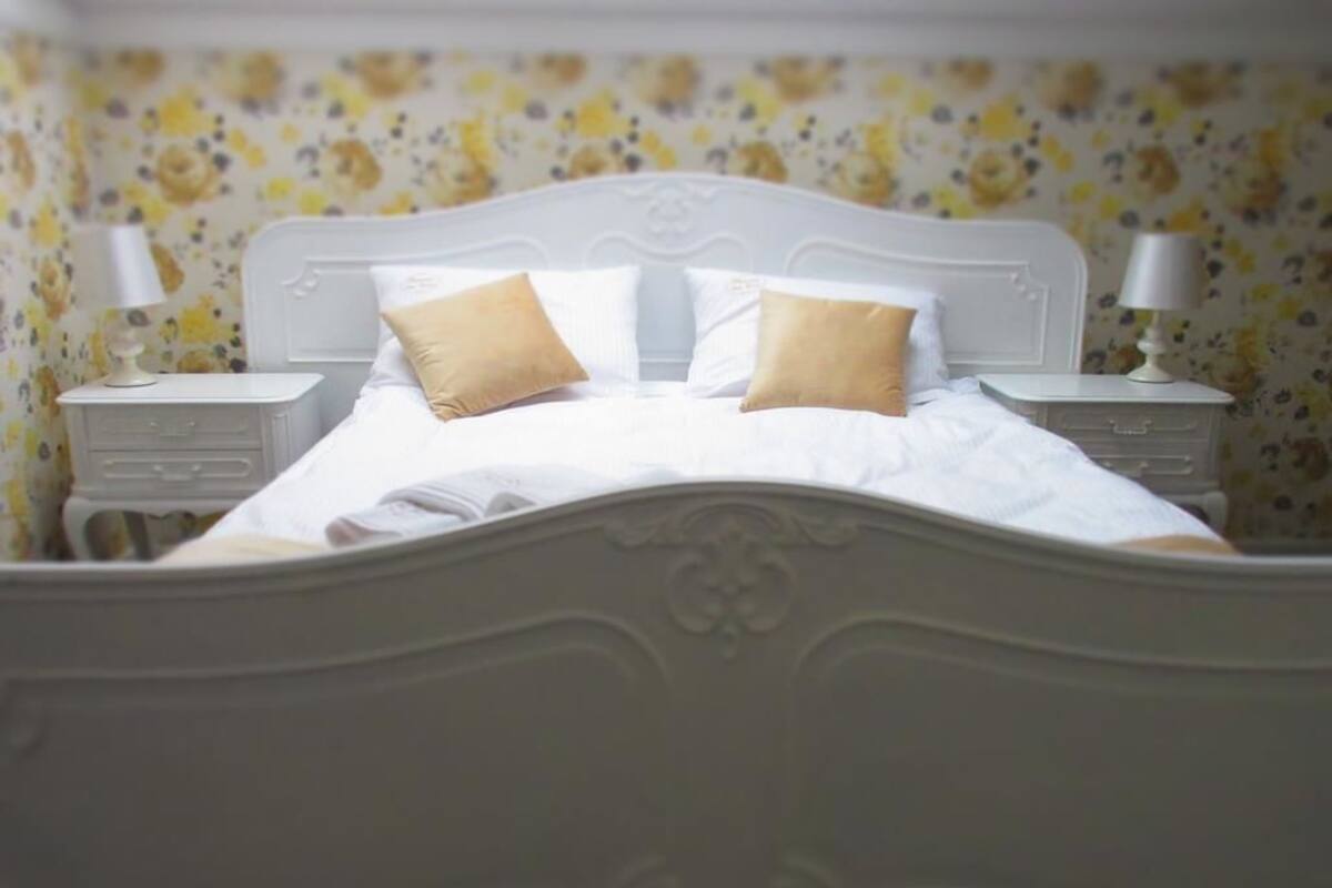 A bed with a white headboard, two bedside tables with lamps, and floral wallpaper.