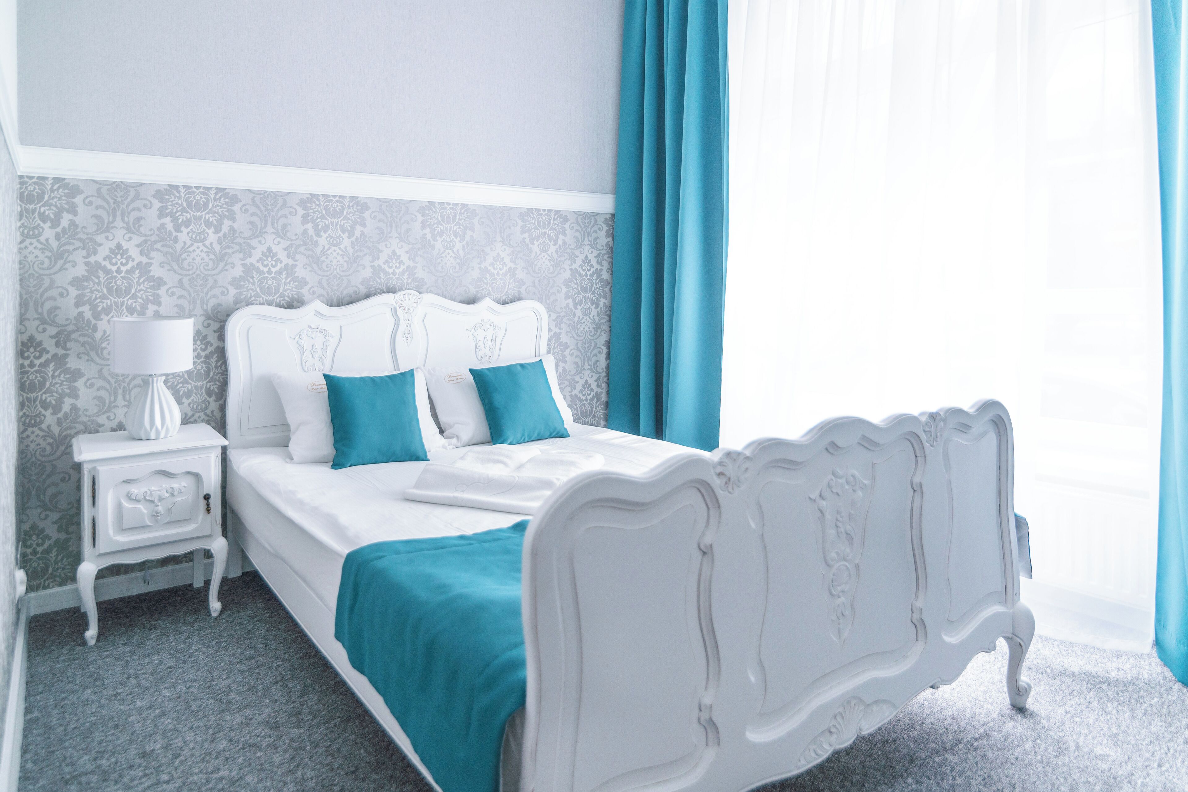 Un dormitorio ordenado con una cama blanca, ropa de cama color aguamarina y una mesita de noche a juego.