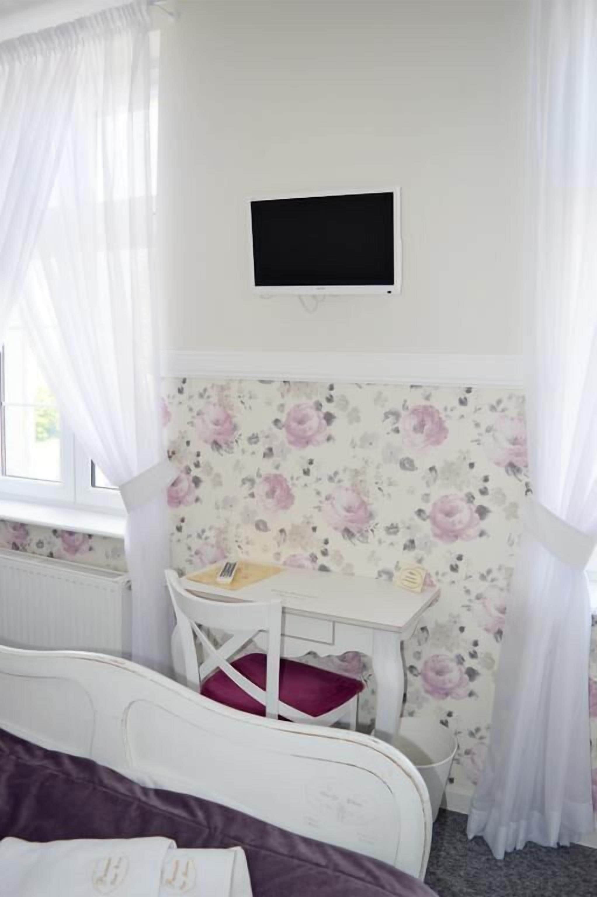 Quarto com cama, uma pequena escrivaninha e televisão na parede.