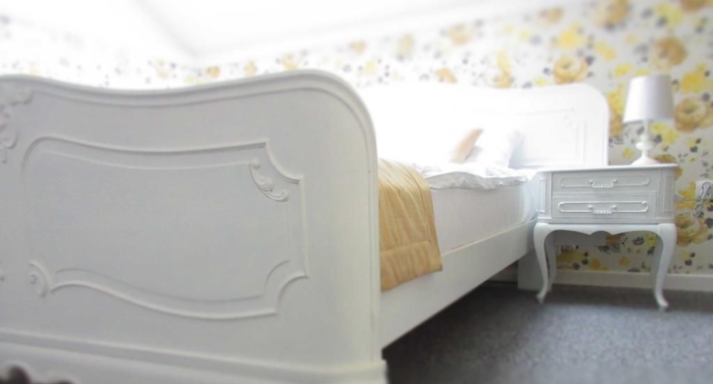 Ein weißes Bett mit Kopfteil, Nachttisch und Lampe.
