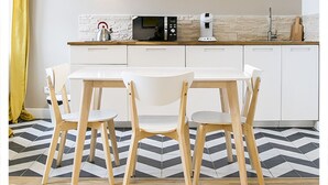 Una cocina moderna con armarios blancos, microondas y cafetera. Hay una mesa de comedor con sillas y una cortina amarilla a la izquierda.