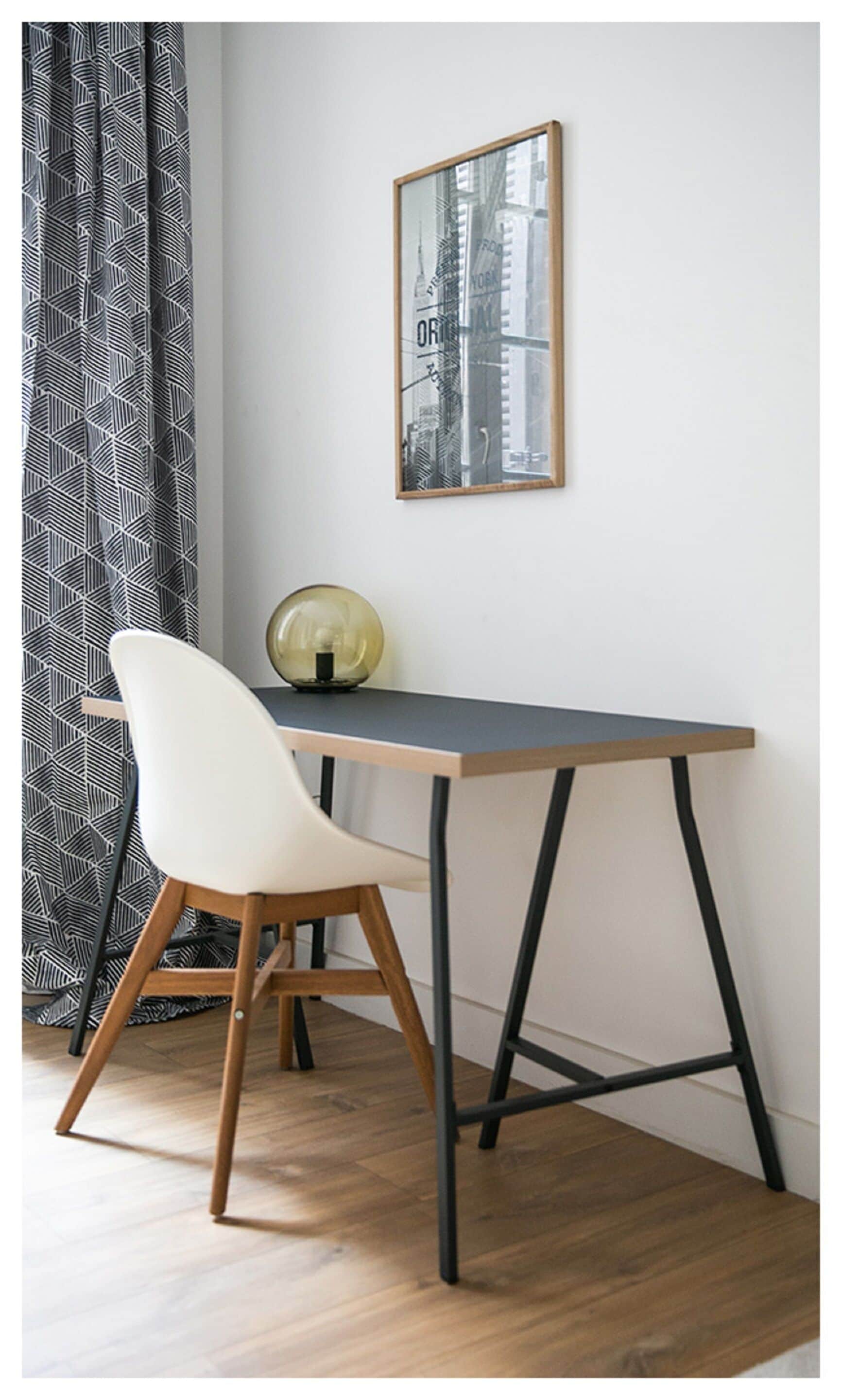 Une pièce d’angle avec un bureau en bois, une chaise blanche, un globe terrestre et, au mur, un tableau représentant une vue panoramique de la ville.