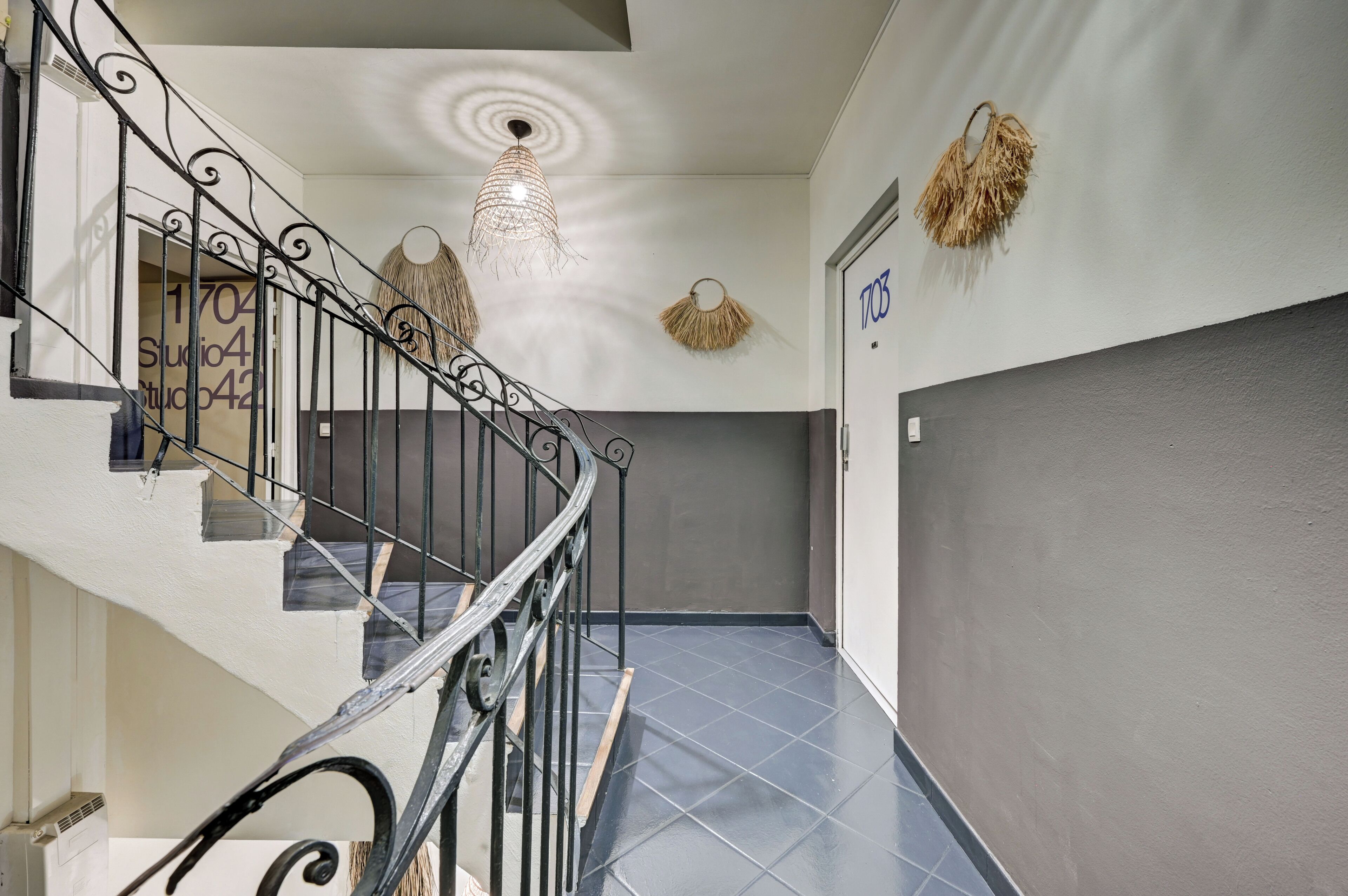 A staircase with a metal railing, a wall-mounted light fixture, and a door with the number '1703' on it.
