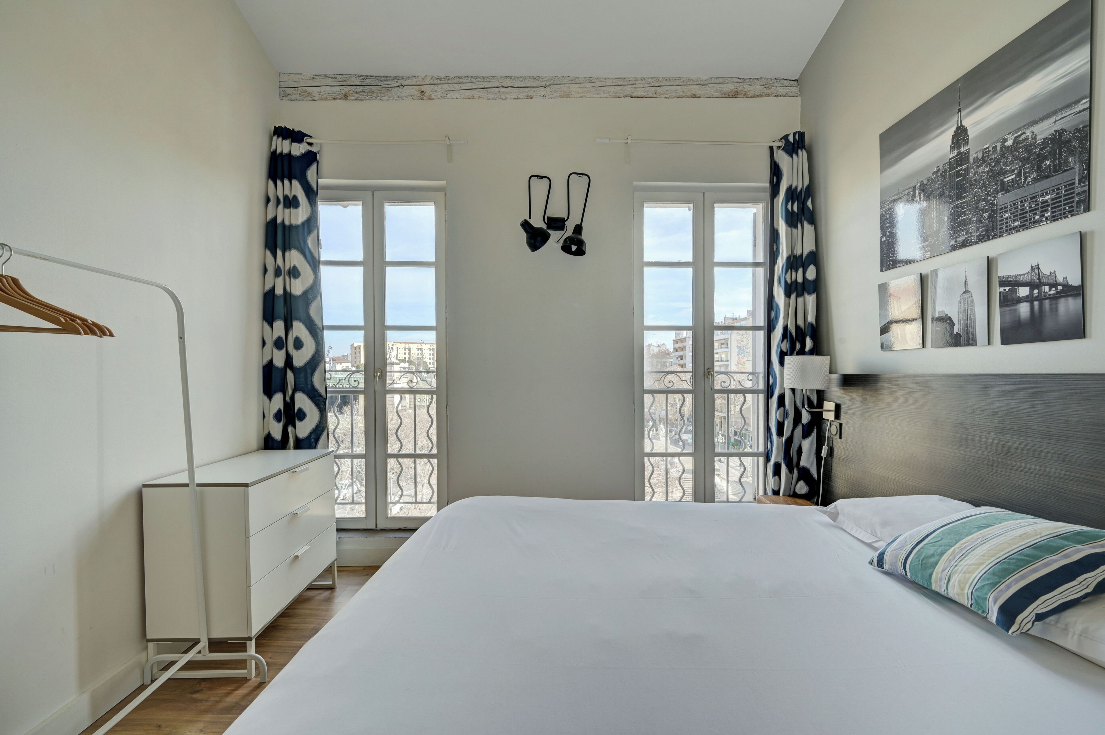 A bedroom with a bed, a dresser, a lamp, and a window with curtains.