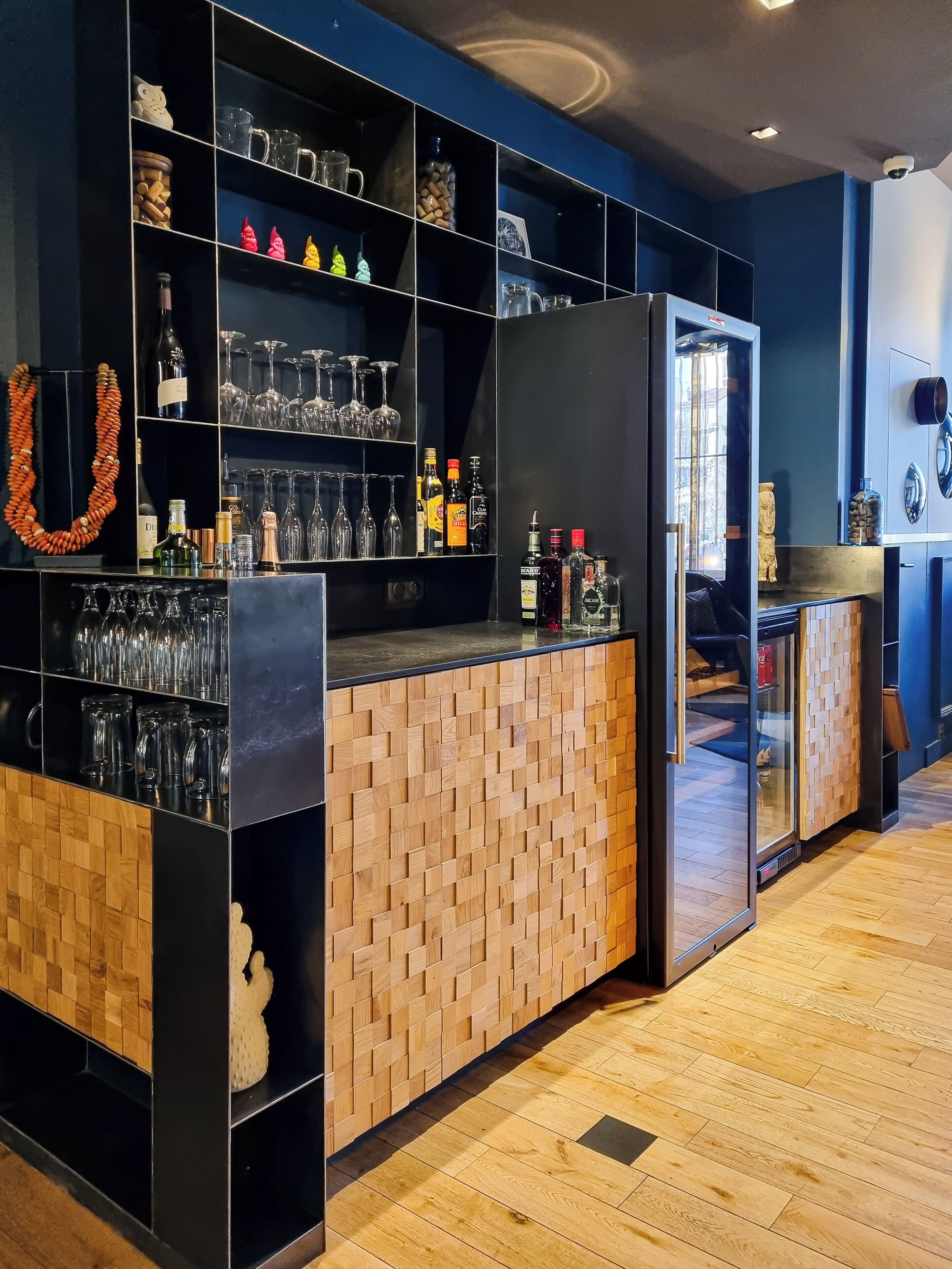 Un espace bar avec des étagères remplies de verres et de bouteilles, un panneau mural en bois et un réfrigérateur.