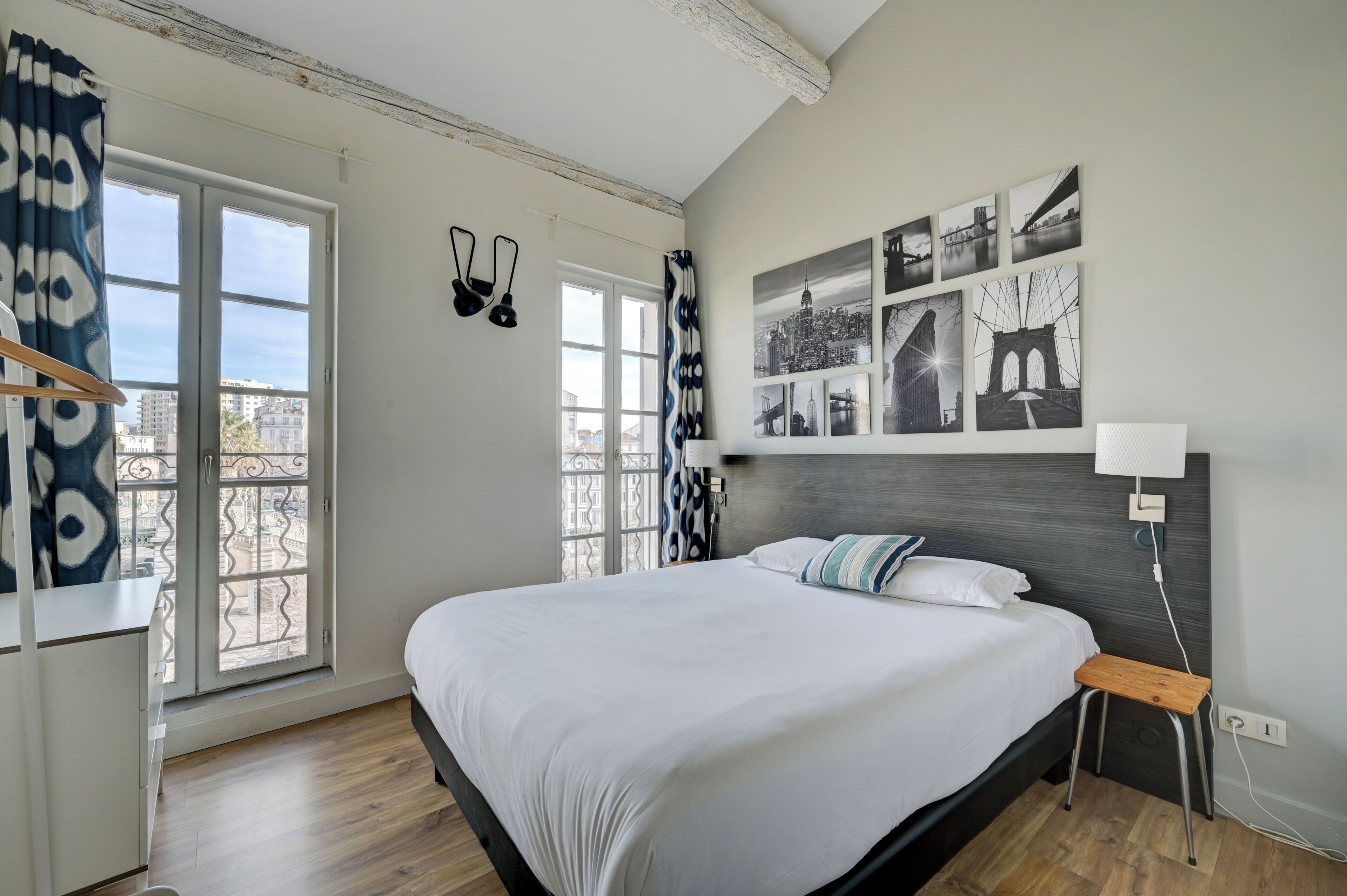 Quarto de hotel com uma cama grande, uma mesa de cabeceira, uma luminária e vista para a cidade pela janela.