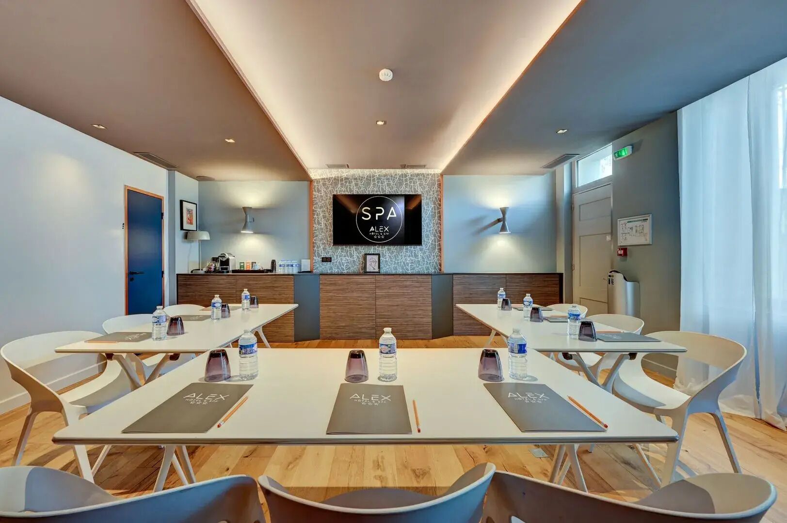 A conference room with a long table, multiple chairs, a TV screen, and a reception desk.