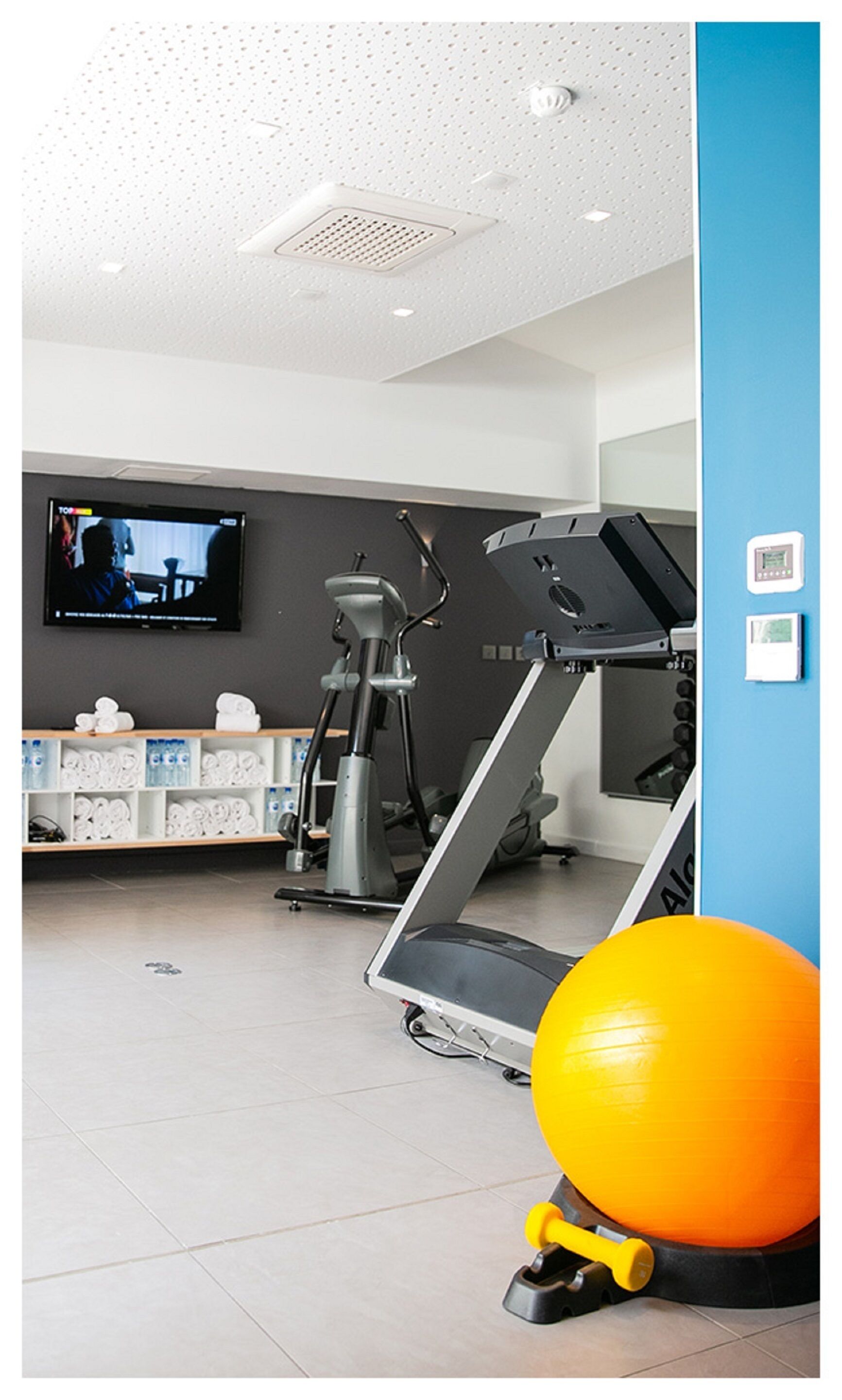 A gym with exercise equipment, a television, and a blue wall.