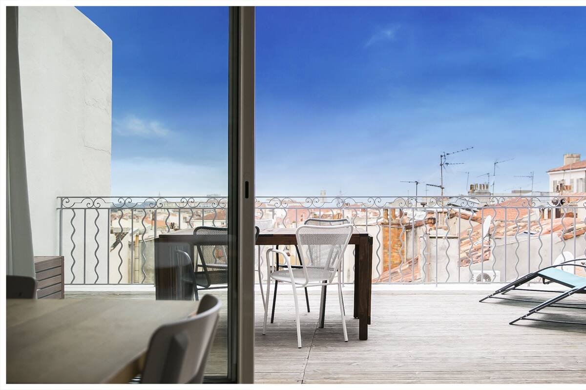 A balcony with a table and chairs, overlooking a cityscape with buildings and antennas.