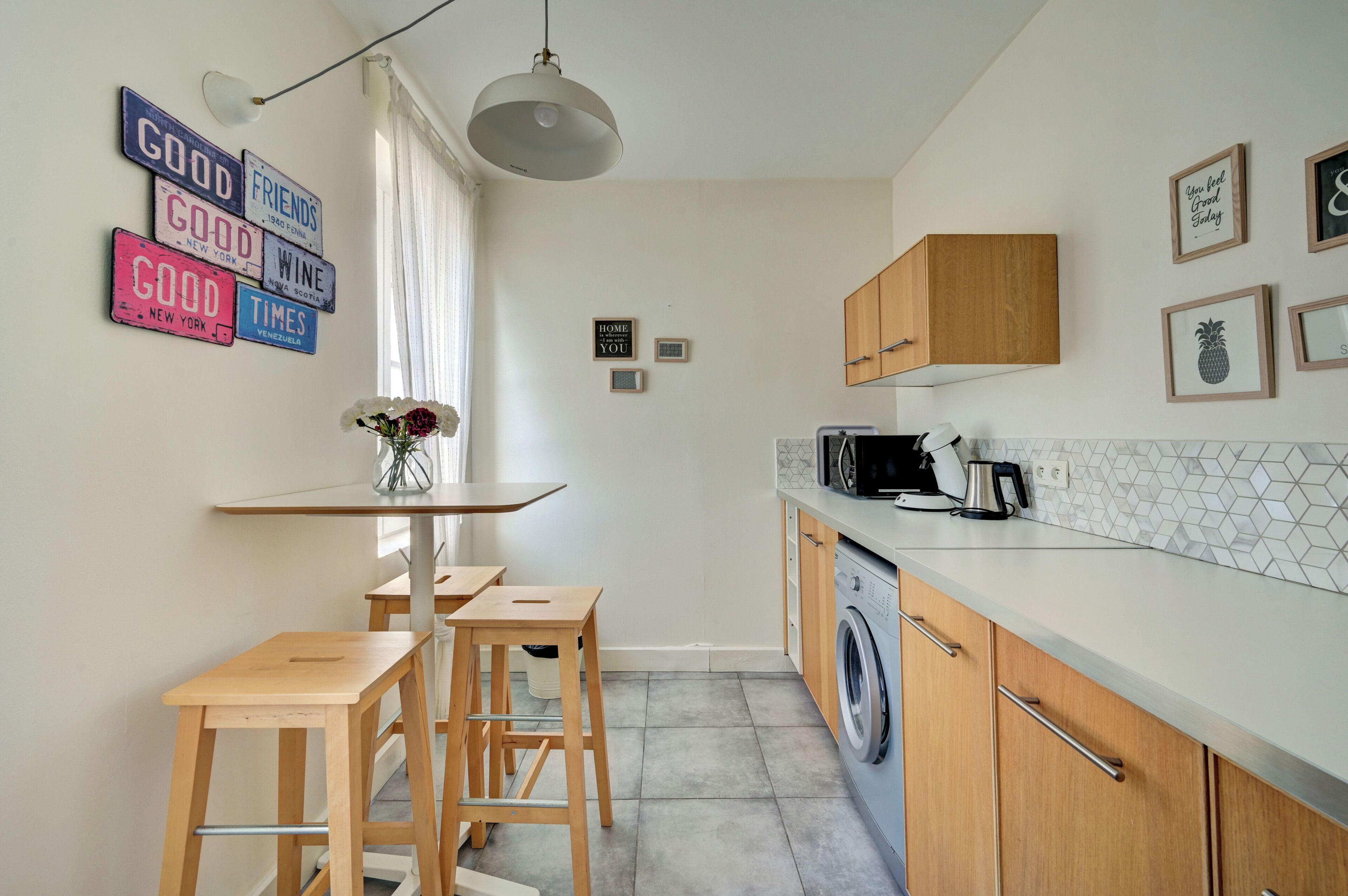 A compact kitchen with wooden stools, a washing machine, and a microwave.