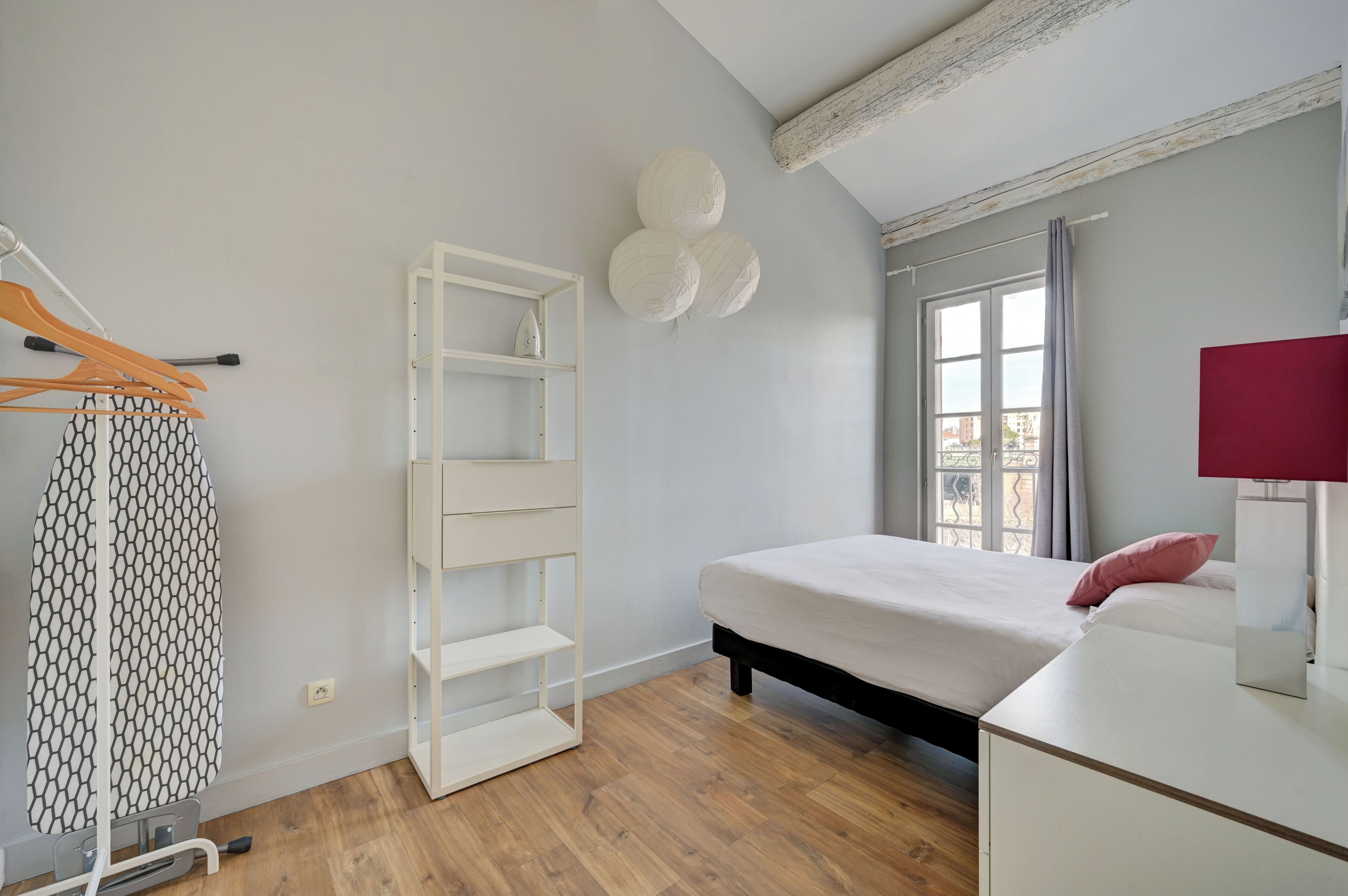 Een slaapkamer met een bed, een kledingkast, een hanglamp en een raam met gordijnen.