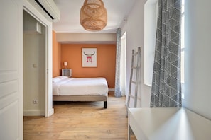 Un dormitorio con cama, mesita de noche, lámpara y una obra de arte en la pared.