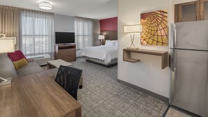 A hotel room with a bed, a desk, a TV, a refrigerator, and a painting on the wall. - Staybridge Suites Florence - Civic Center by IHG (Florence)
