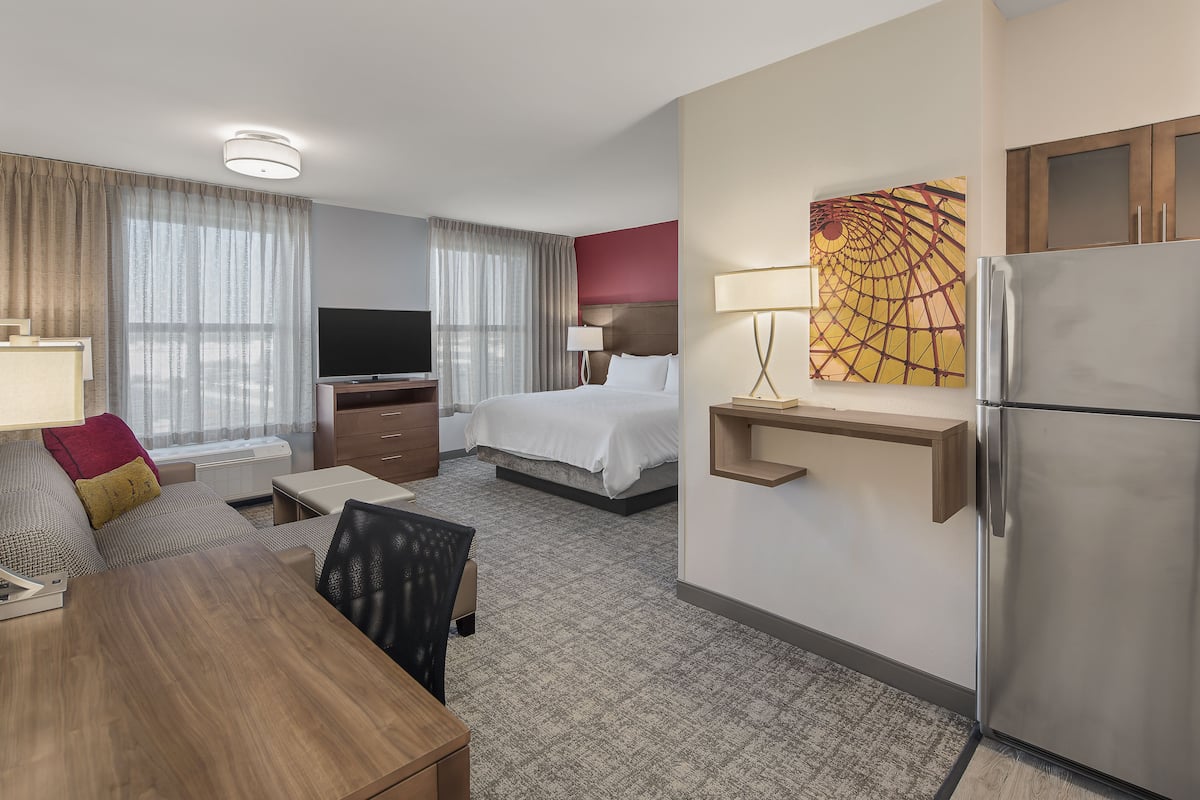 A hotel room with a bed, a desk, a TV, a refrigerator, and a painting on the wall.