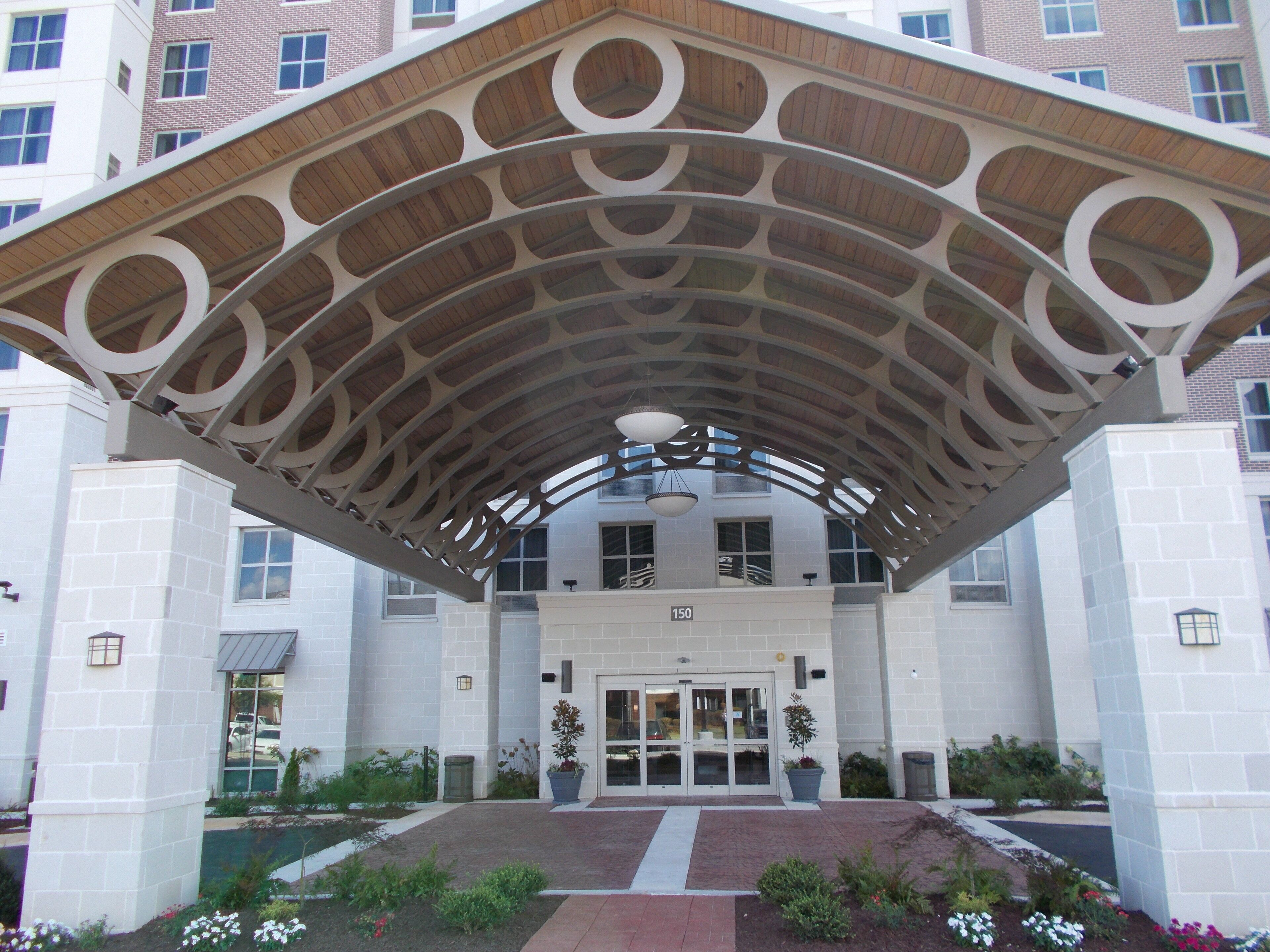 A building with a distinctive arched entrance canopy, a numbered entrance, and a landscaped garden area.