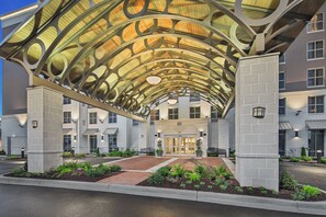 A hotel entrance with a covered walkway, a brick pathway, and a well-maintained garden. - Staybridge Suites Florence - Civic Center by IHG (Florence)