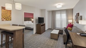 A hotel room with a dining area, a bed, a TV, a sofa, and a desk. - Staybridge Suites Florence - Civic Center by IHG (Florence)