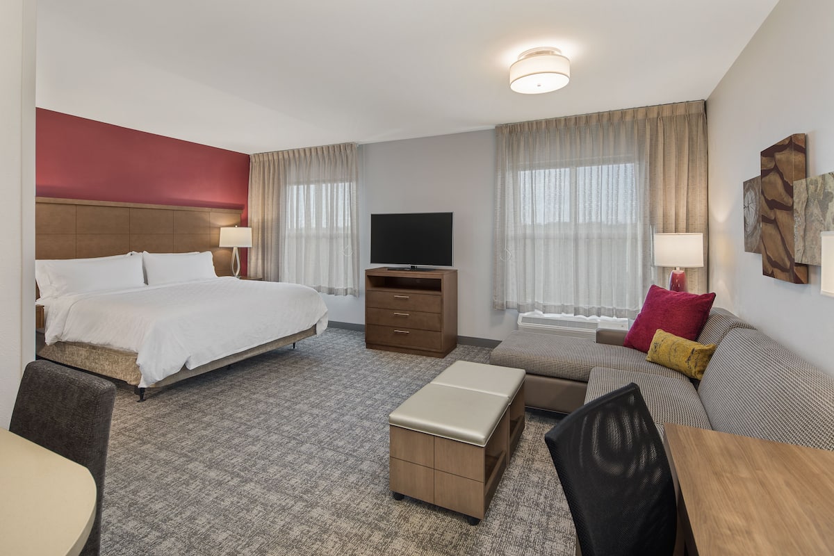 A hotel room with a large bed, a sofa, a TV, a desk, and a small table.