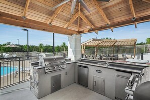 An outdoor kitchen area with a grill, a pool, and a covered seating area. - Staybridge Suites Florence - Civic Center by IHG (Florence)