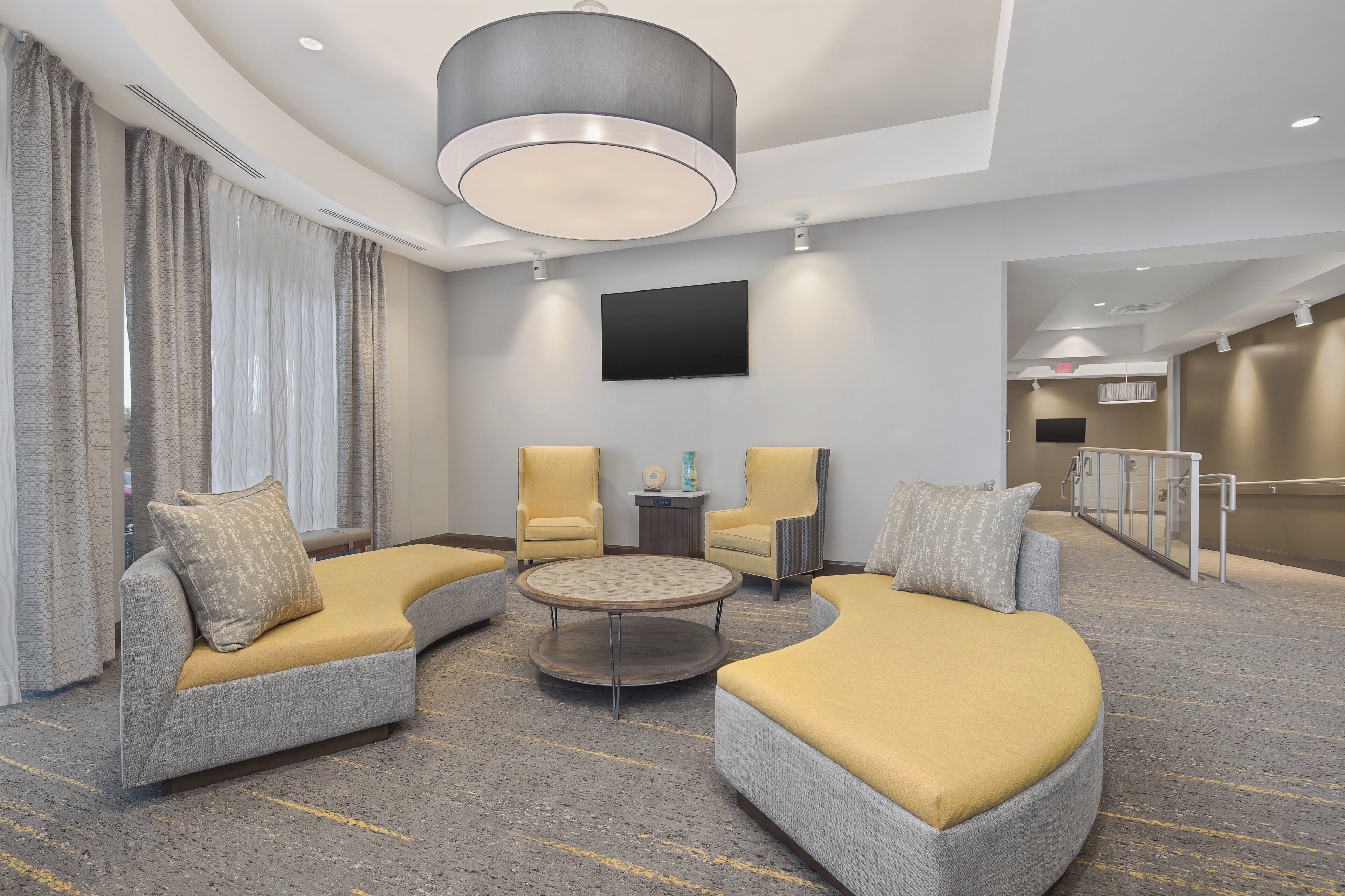 A modern hotel lobby with a seating area, a flat-screen TV, and a staircase.
