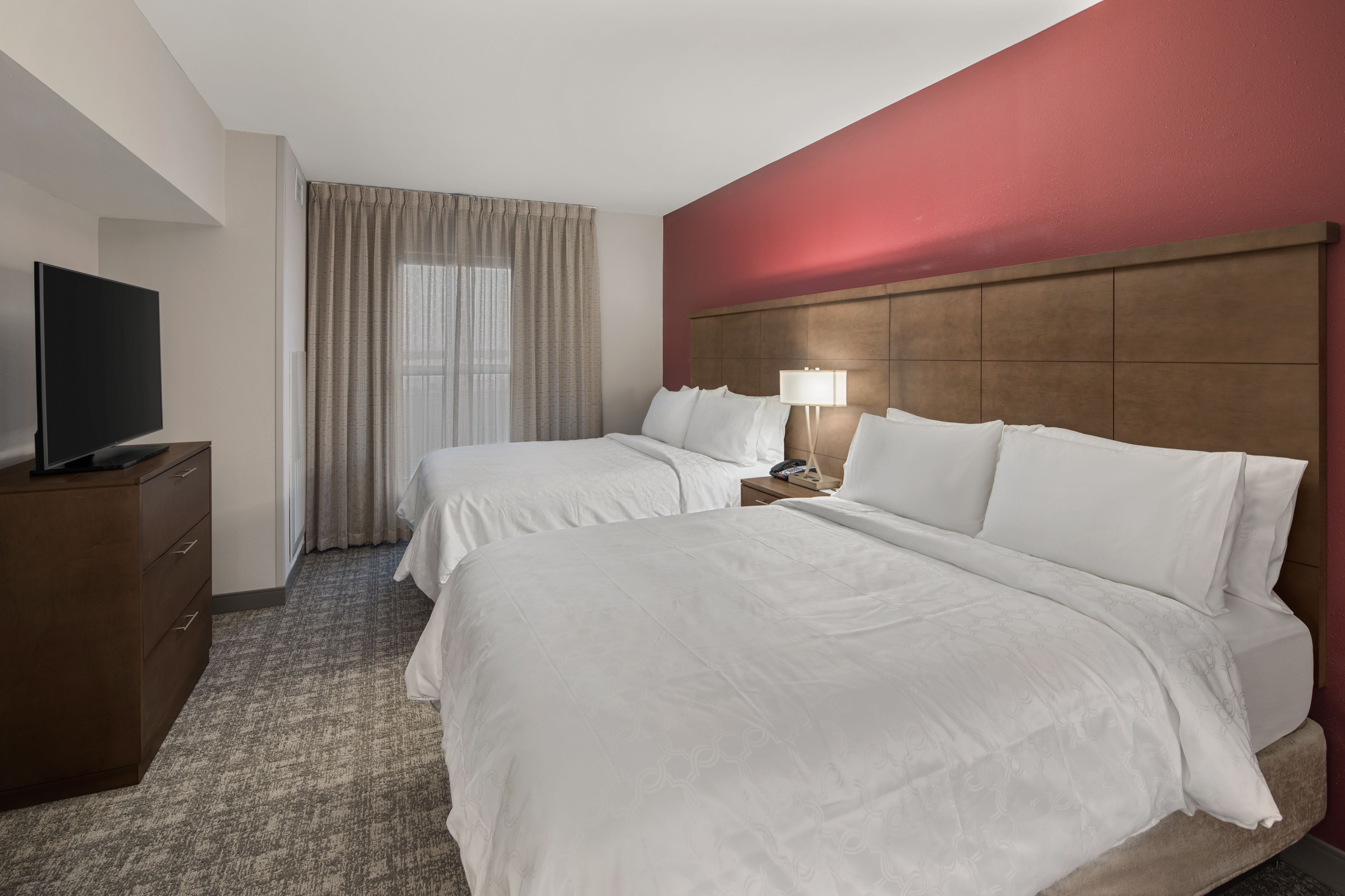 A hotel room with two beds, a TV, a lamp, and a wooden headboard.