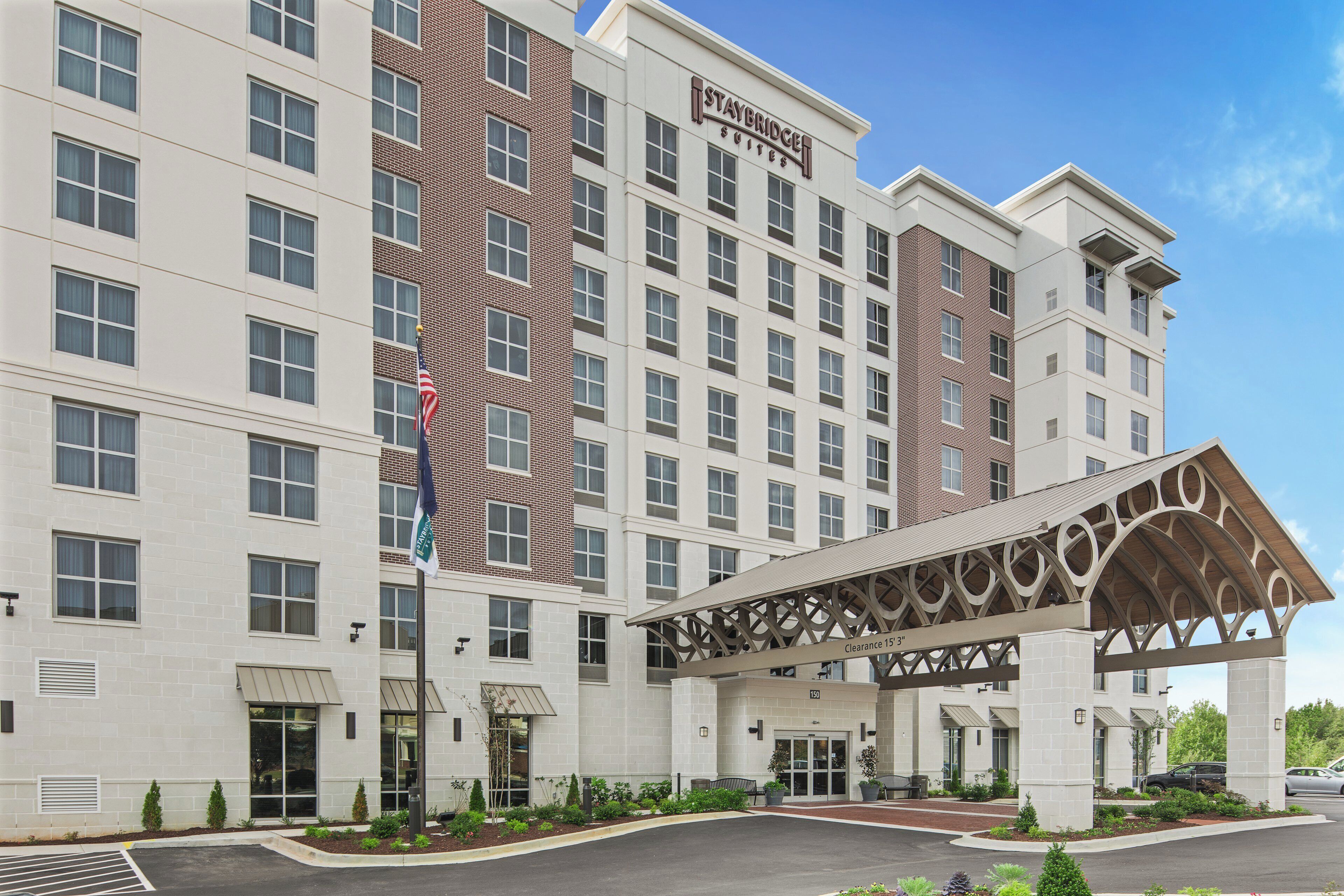 A multi-story hotel with a prominent Staybridge Suites sign, a covered entrance, and a parking area.