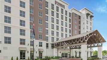 Un hotel de varios pisos con un llamativo letrero de Staybridge Suites, un acceso cubierto y un área de estacionamiento.