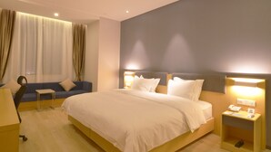 Habitació d'hotel amb un llit gran, un sofà, una taula de treball i una cambrera de nit amb un telèfon.