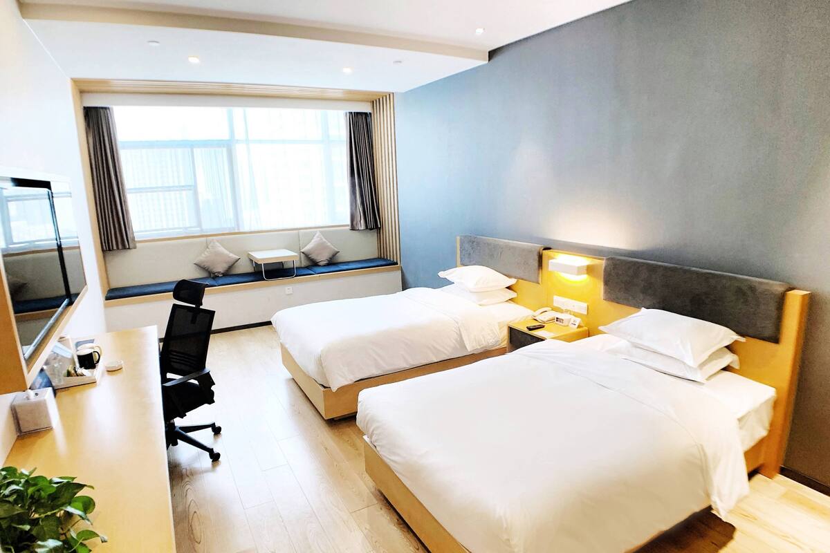 A hotel room with two beds, a desk, a chair, a small table, and a window with curtains.