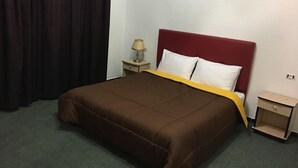 Une chambre d’hôtel avec un lit simple, une table de chevet, une lampe et un rideau.