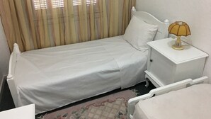Une petite chambre avec un lit simple, un chevet muni d’une lampe et une fenêtre avec des rideaux.