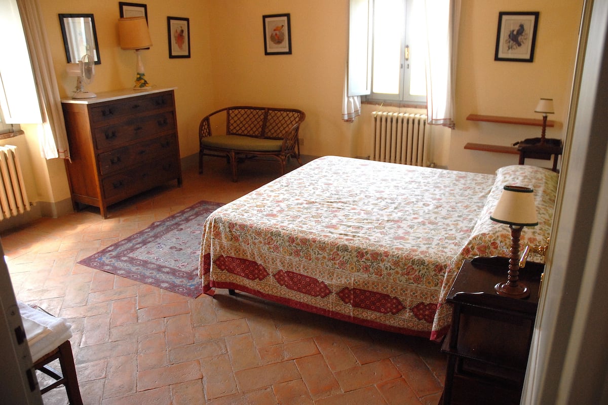A bedroom with a bed, dresser, chair, and a radiator.