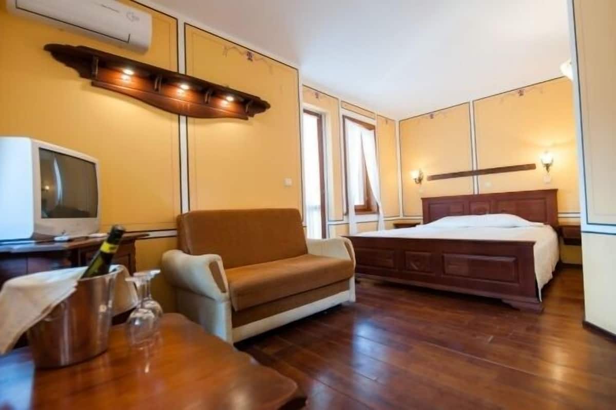 Une chambre d’hôtel avec un plancher en bois, un lit avec une tête de lit en bois, un canapé, une télévision et un minibar.