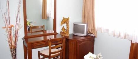 A room with a wooden desk, a chair, a television, a mirror, and a vase with flowers.