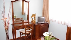 Ein Zimmer mit Schreibtisch aus Holz, einem Sessel, einem Fernseher, einem Spiegel und einer Vase mit Blumen.