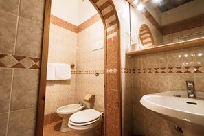 A bathroom with two toilets, a sink, and a shower area.