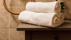 A bathroom with a wooden towel ring, two rolled towels, and a vase with white flowers on a wooden counter.