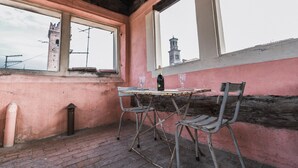 A rustic room with a brick floor, a table with two chairs, a bottle, and two glasses. A window reveals a tower in the background.