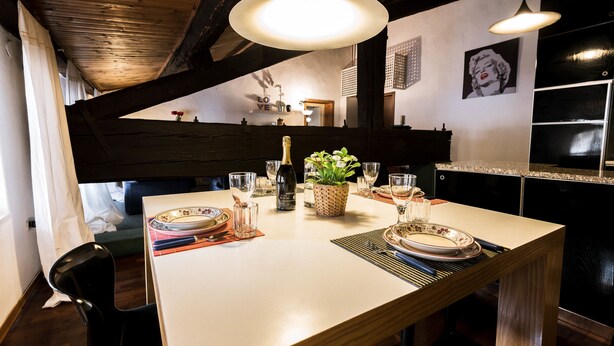 A dining area with a wooden table set for two, a potted plant, and a bottle of champagne.