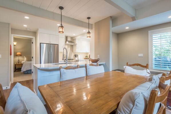 A modern kitchen with stainless steel appliances, a wooden dining table, and pendant lighting.