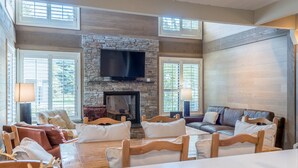 Un salón amplio con chimenea de piedra, un televisor de pantalla plana grande y una zona de estar cómoda con sofá y sillones.