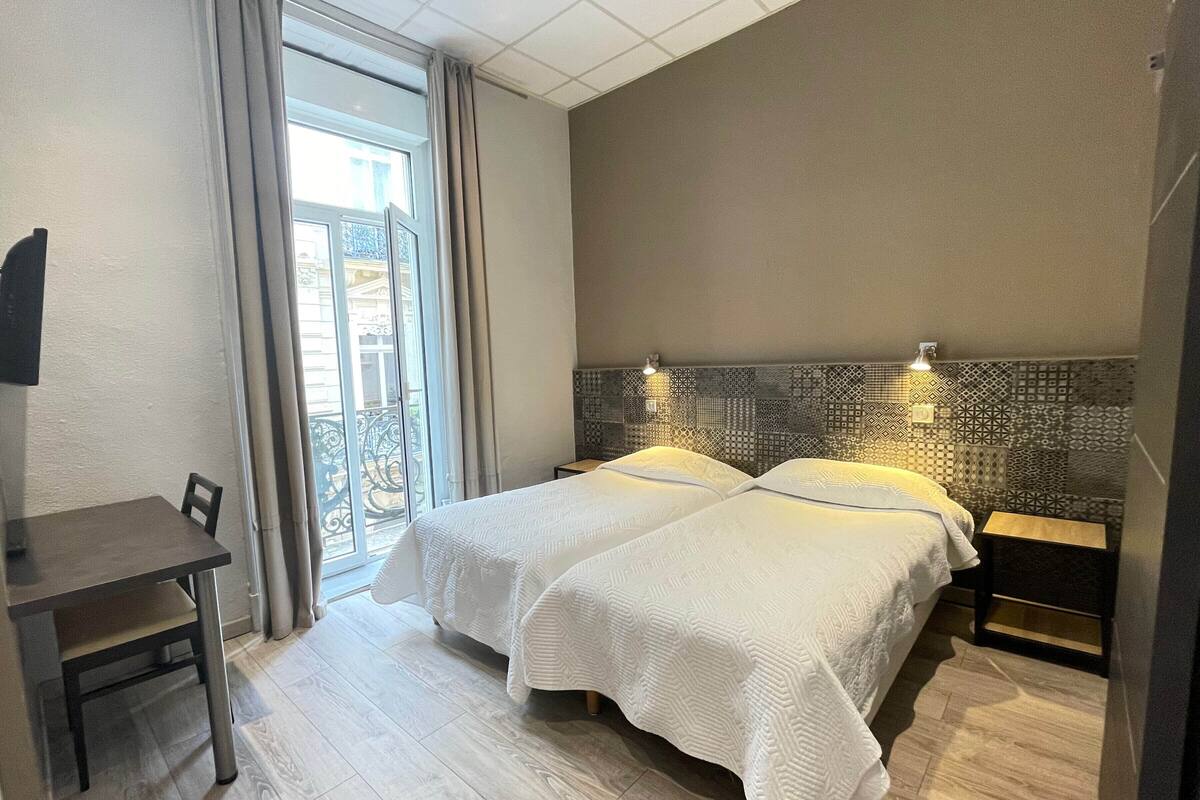 A hotel room with two beds, a desk, and a view of a balcony.