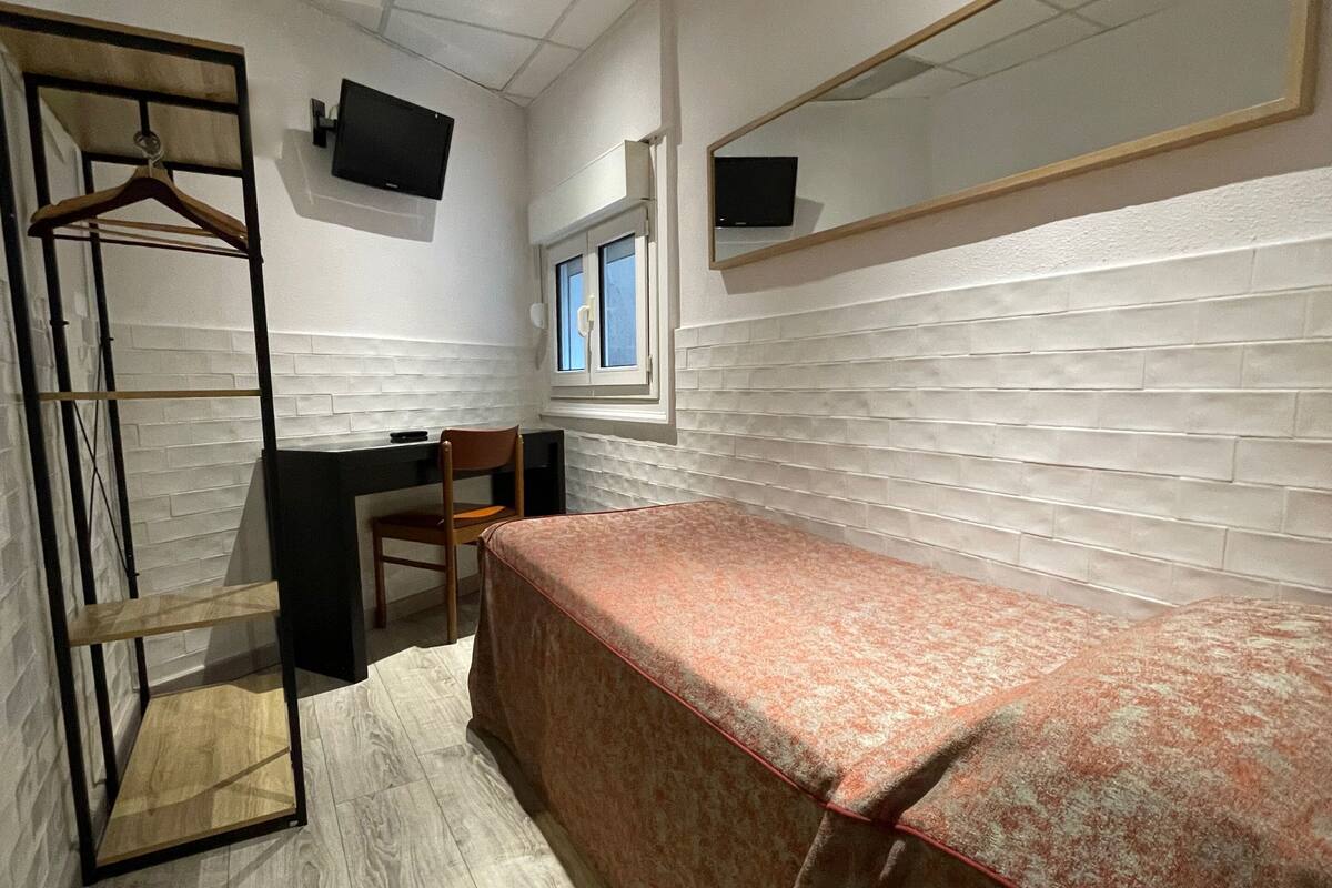 A bedroom with a bed, a desk, a chair, a wardrobe, and a TV mounted on the wall.