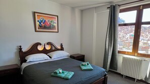 Una habitación de hotel con cama, un cuadro en la pared, una ventana con vistas y un radiador.