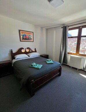 Una habitación de hotel con cama, un cuadro en la pared, una ventana con vistas y un radiador.