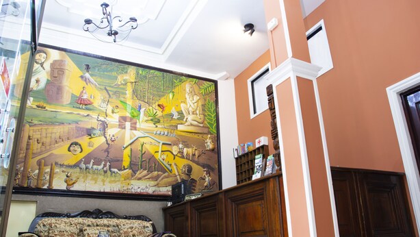 Una habitación con un mural grande, un banco de madera y una estantería con objetos.