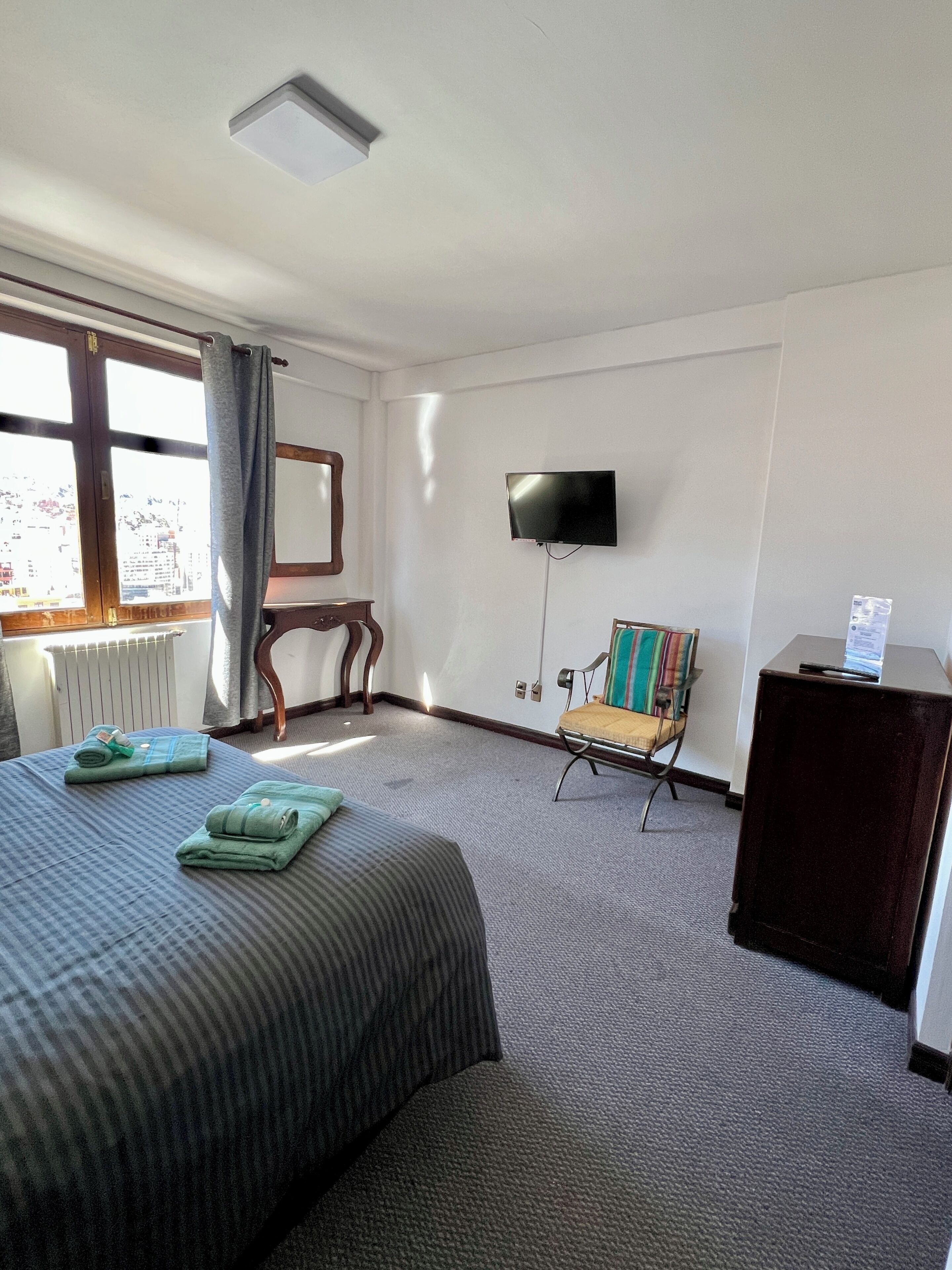 Quarto de hotel com cama, televisão, cadeira e escrivaninha.